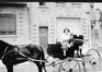 Photo Femme et enfant (mère et fils ?) dans une voiture à cheval, devant l'immeuble Rue du Gulden Bodem, 19 (Molenbeek-Saint-Jean), photogr. anon., s.d. [années 1930].<br>